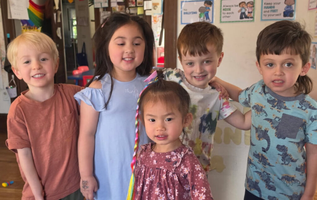 Four smiling children with their arms around each other outdoors