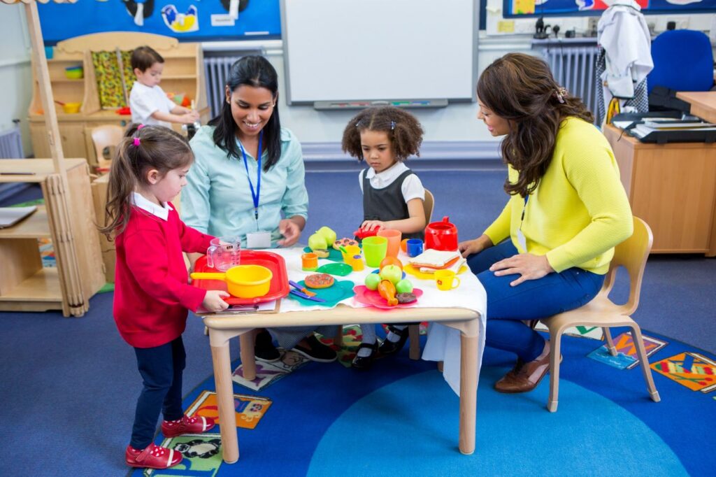 Two educators playing pretend kitchen with preschoolers